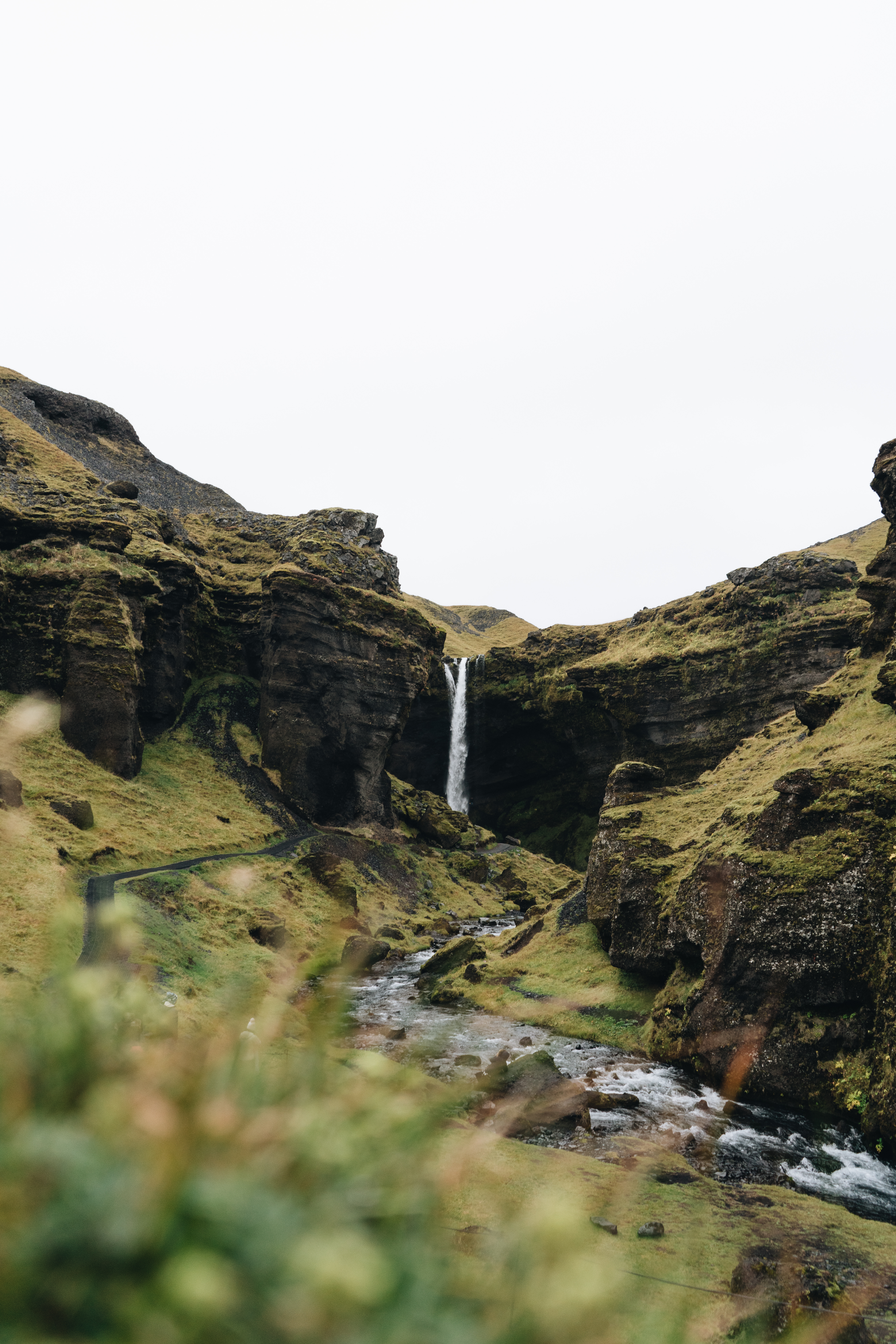 Dramatic waterfall Kvernufoss cascading down moss-covered volcanic cliffs in Iceland, with rushing stream and green vegetation in foreground