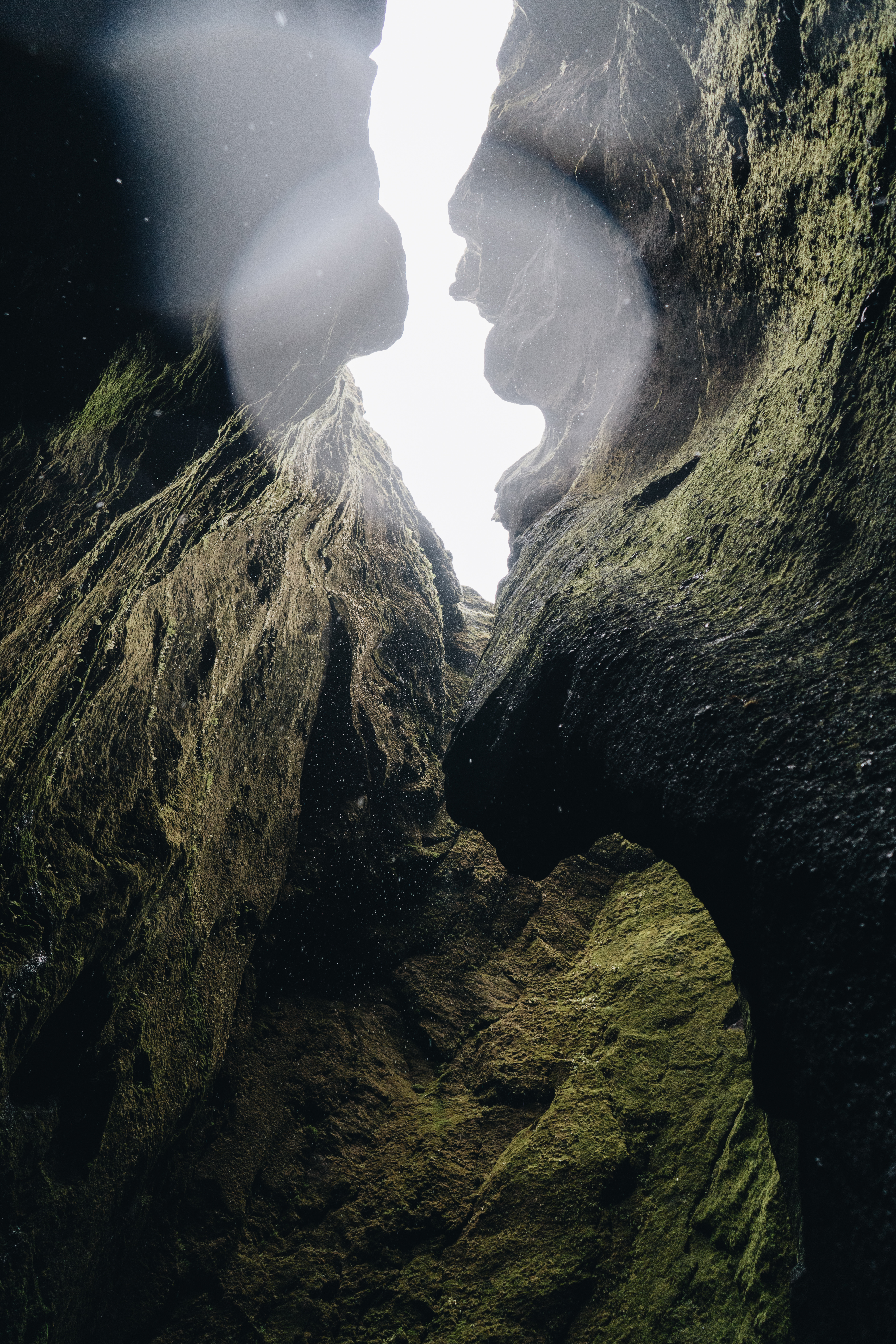 Sunlight streaming through narrow canyon opening in Hvolsvöllur Iceland, illuminating moss-covered volcanic rock walls with dramatic natural light flares and textured geological formations