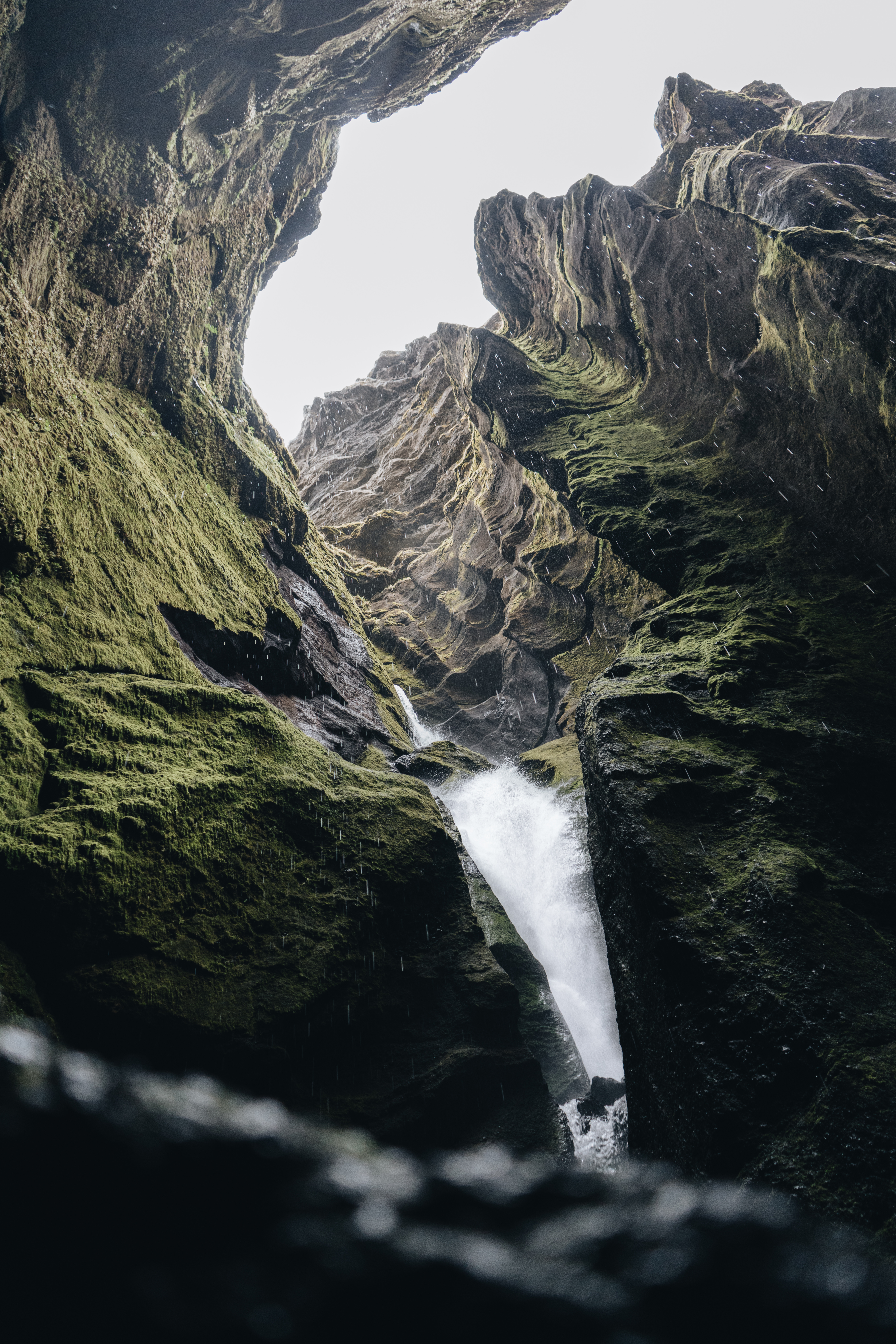 Powerful waterfall cascading through layered rock formations in Hvolsvöllur Iceland, featuring moss-covered cliffs and dramatic geological striations in the canyon walls