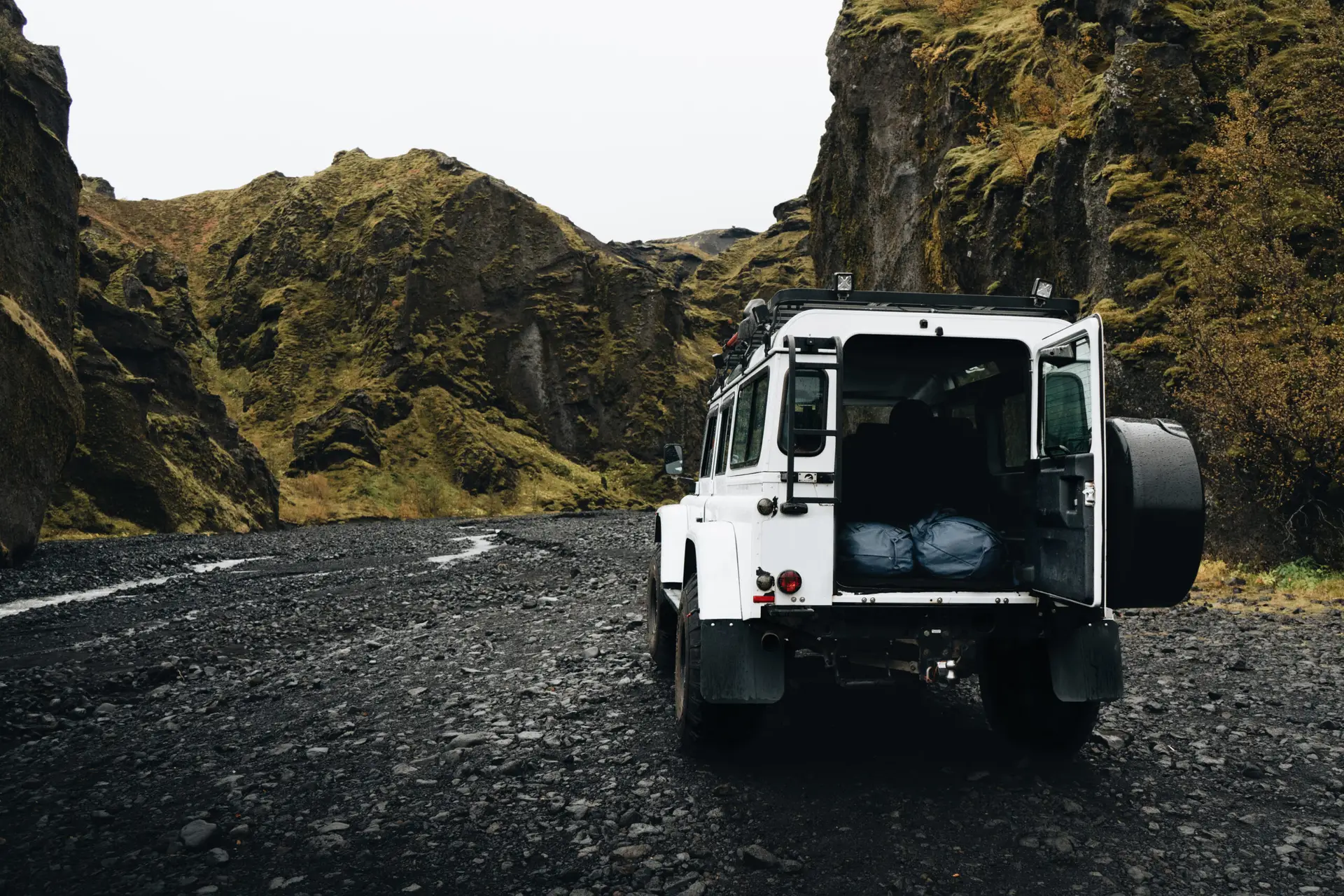White off-road vehicle parked on a rugged black gravel road surrounded by cliffs