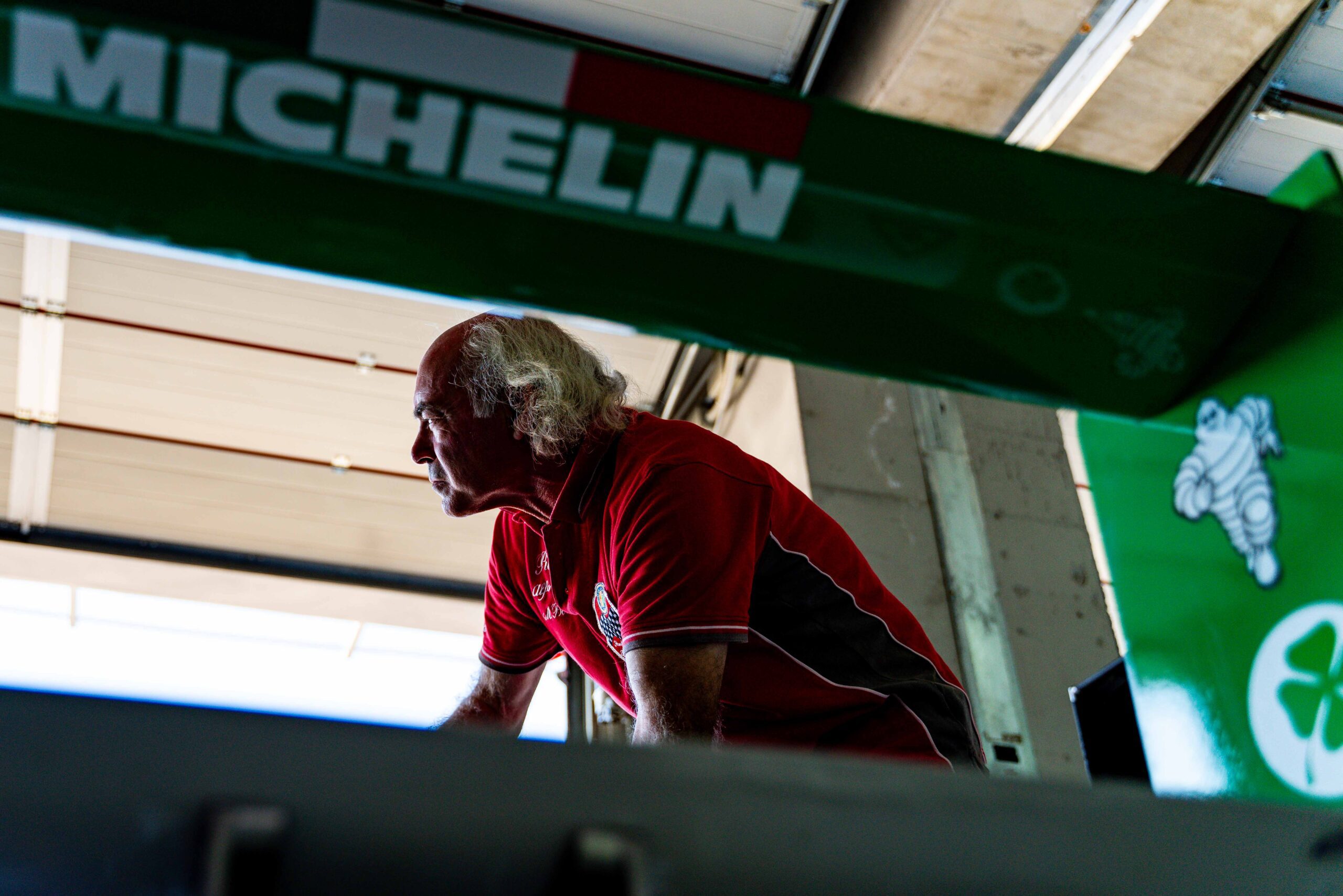 Portrait of a team member in a red shirt seen through a green Michelin-branded frame in a garage