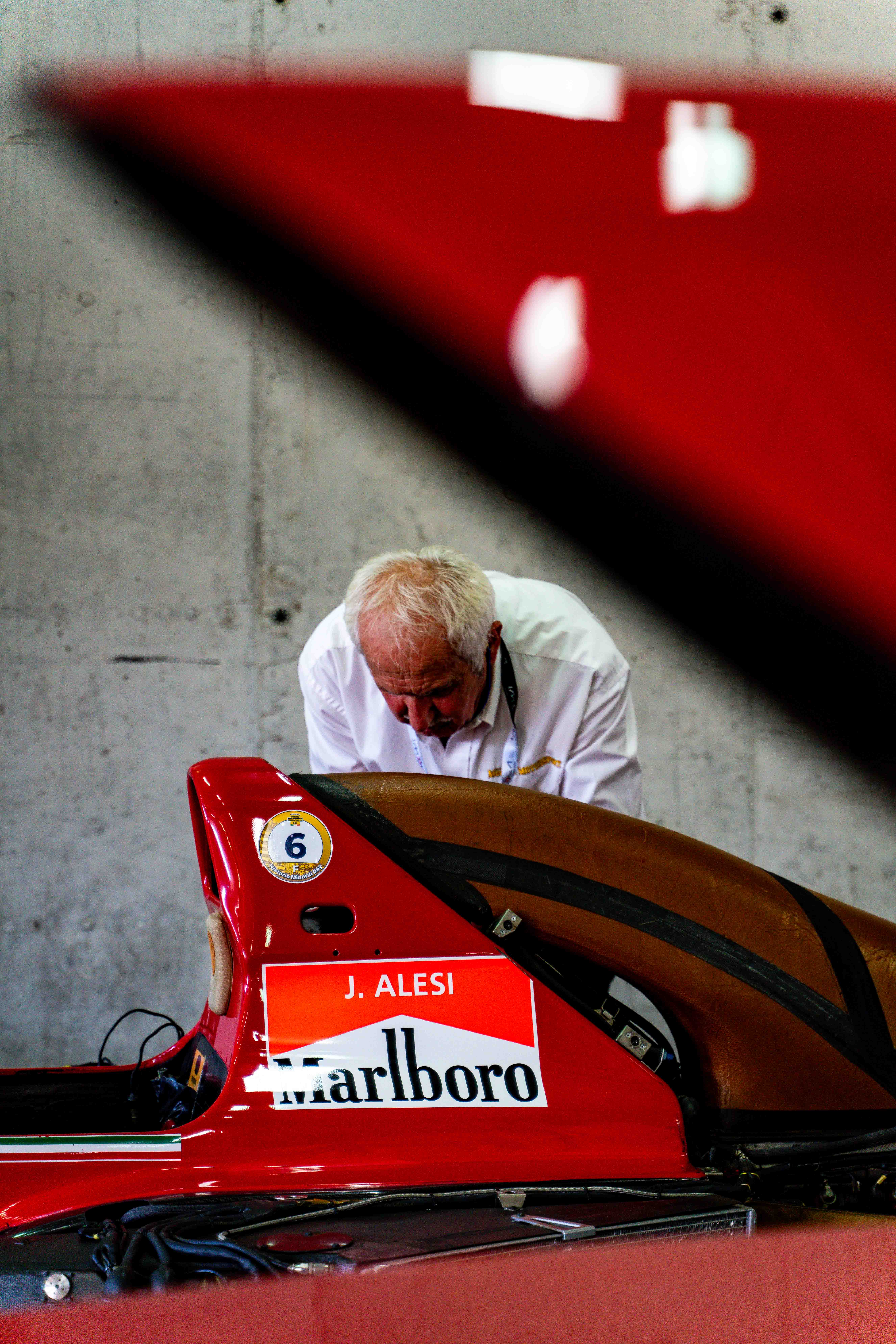 Mechanic working on a red Ferrari Formula 1 car bearing “J. Alesi” and Marlboro branding