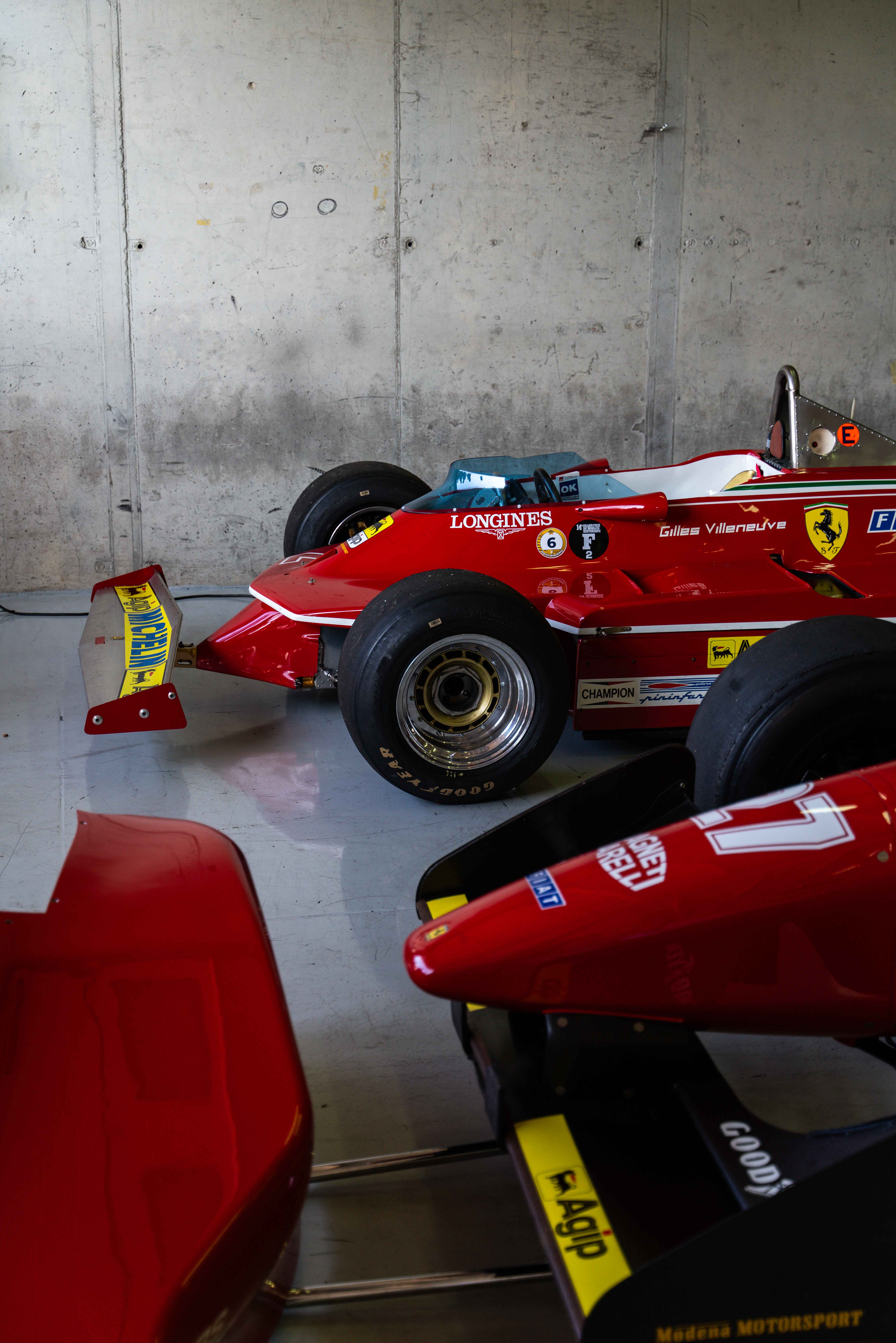 Two vintage Ferrari Formula 1 cars displayed in a garage, highlighting their iconic red color