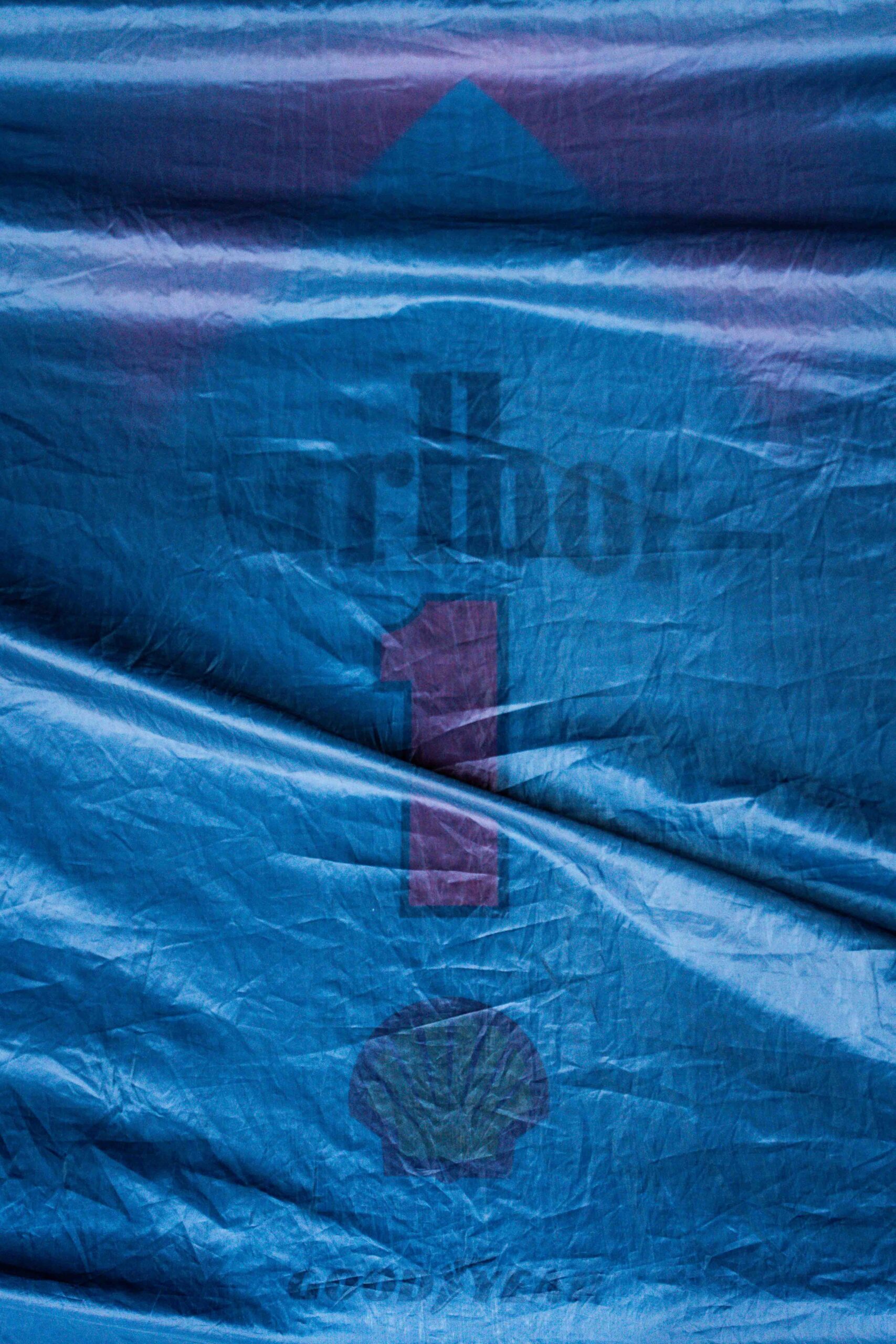Close-up of a blue racing cover featuring a faded “number 1” symbol with logos underneath, draped over a structure