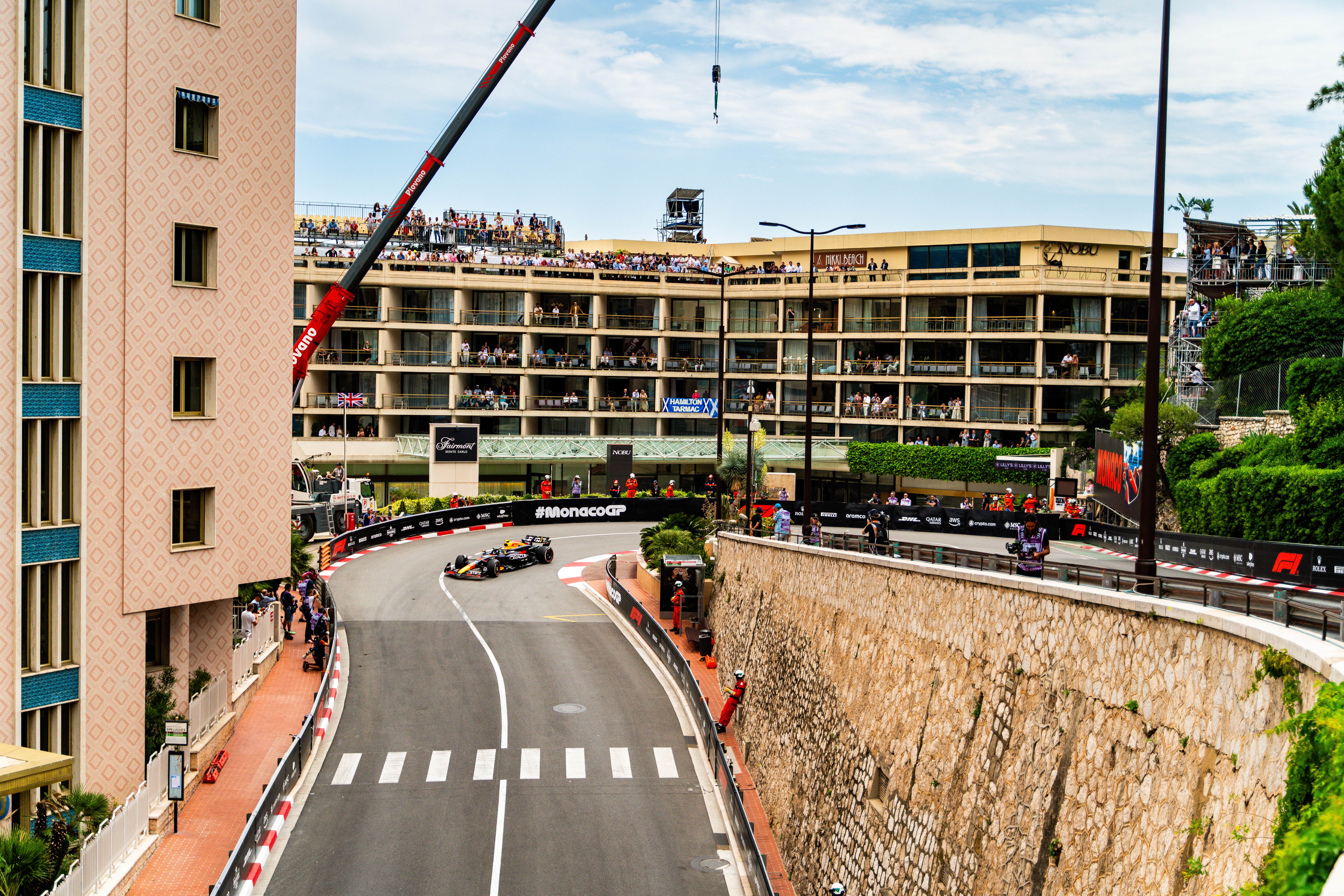 Formula 1 cars racing through a winding section of the Monaco circuit with packed grandstands and urban buildings in the background
