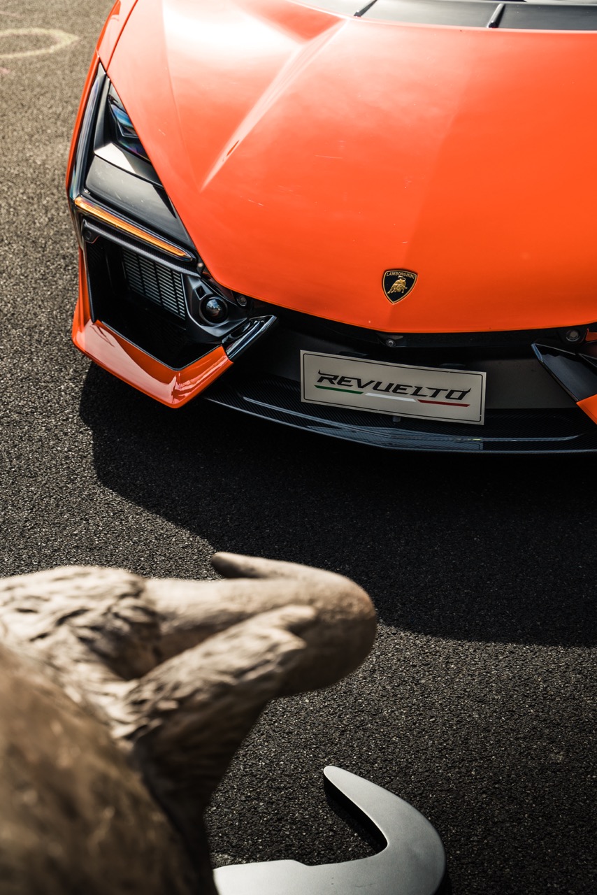Close-up of an orange Lamborghini front grille, with a bull statue in the foreground, showcasing the brand’s iconic design