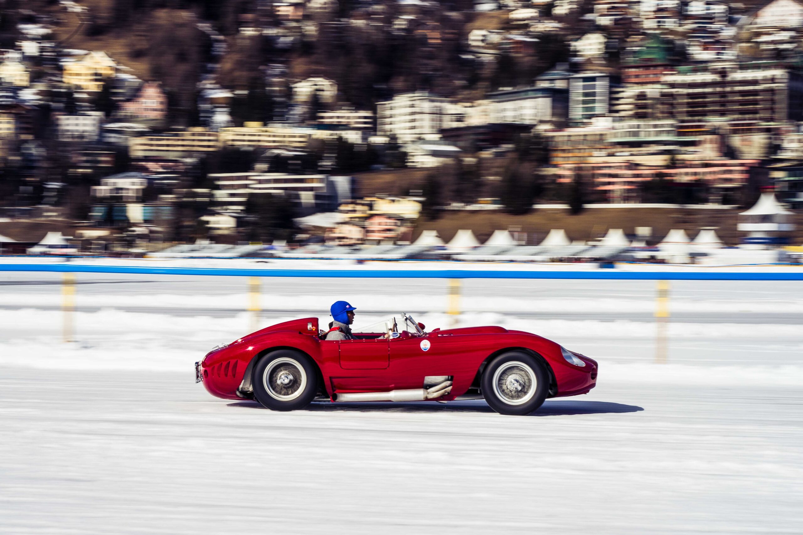 Red vintage race car in motion on a snowy track at The I.C.E. St. Moritz 2023, showcasing classic automotive elegance
