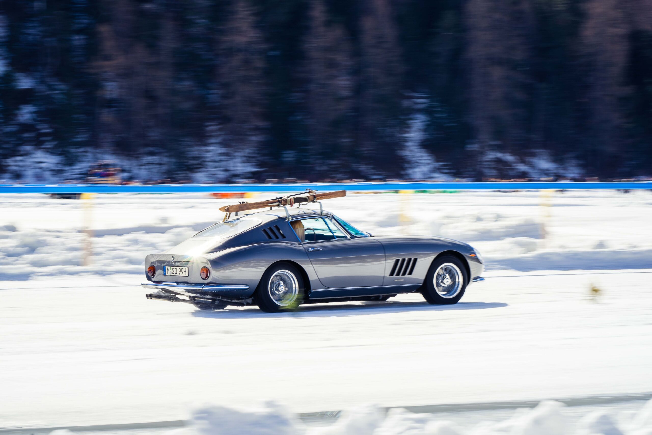 Silver vintage Ferrari with wooden skis on the roof rack, driving on ice at The I.C.E. St. Moritz 2023