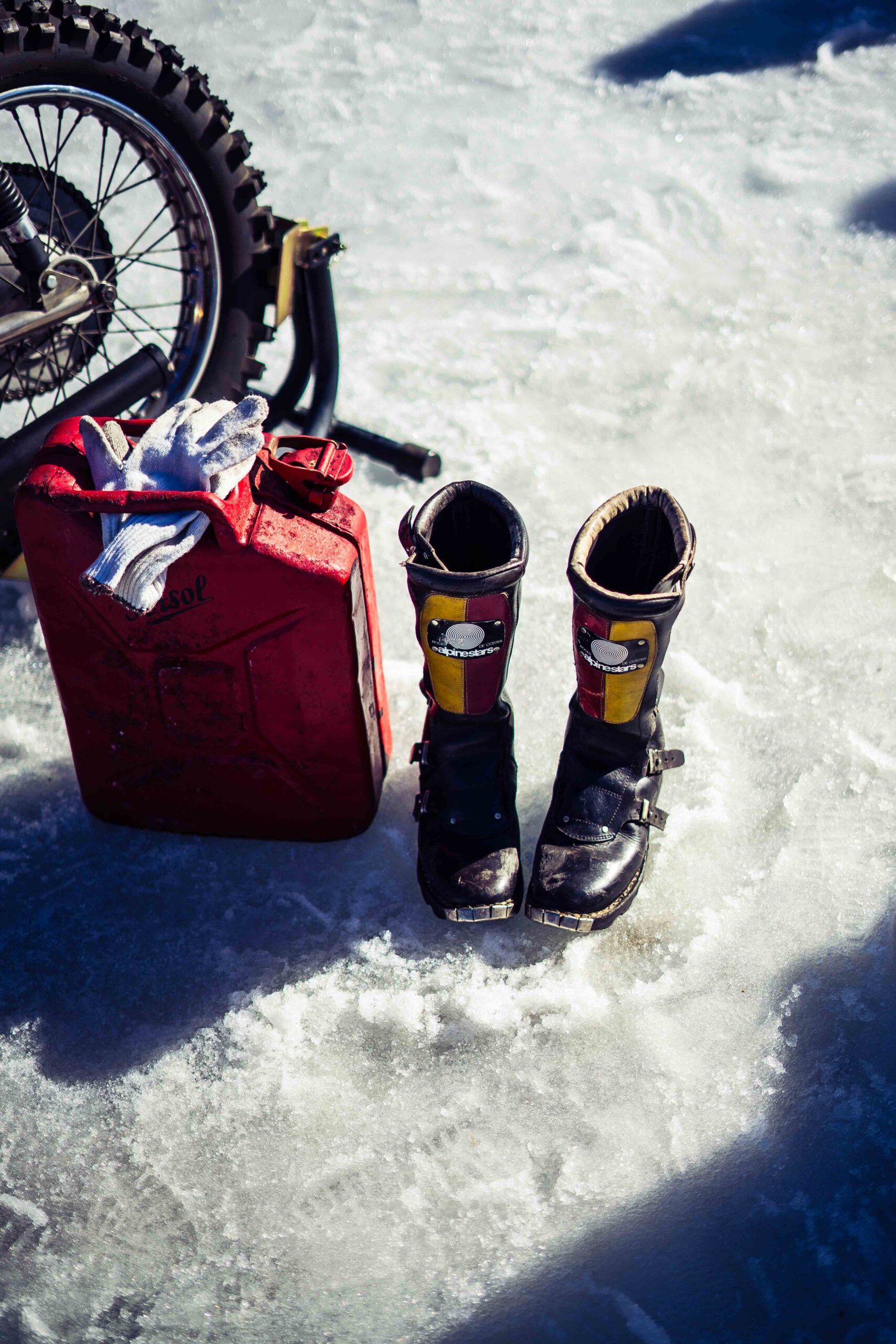 Motorcycle boots, a red fuel canister, and gloves placed on an icy surface during The I.C.E. St. Moritz 2023 event