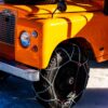 Close-up of an orange Land Rover with snow chains on tires, photographed at The I.C.E. St. Moritz 2023 on an icy terrain
