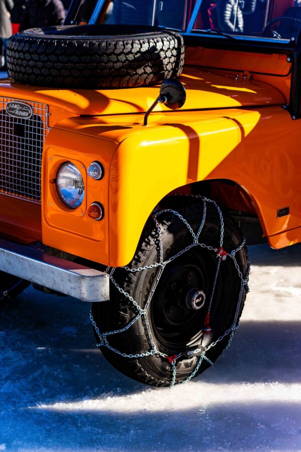 Close-up of an orange Land Rover with snow chains on tires, photographed at The I.C.E. St. Moritz 2023 on an icy terrain