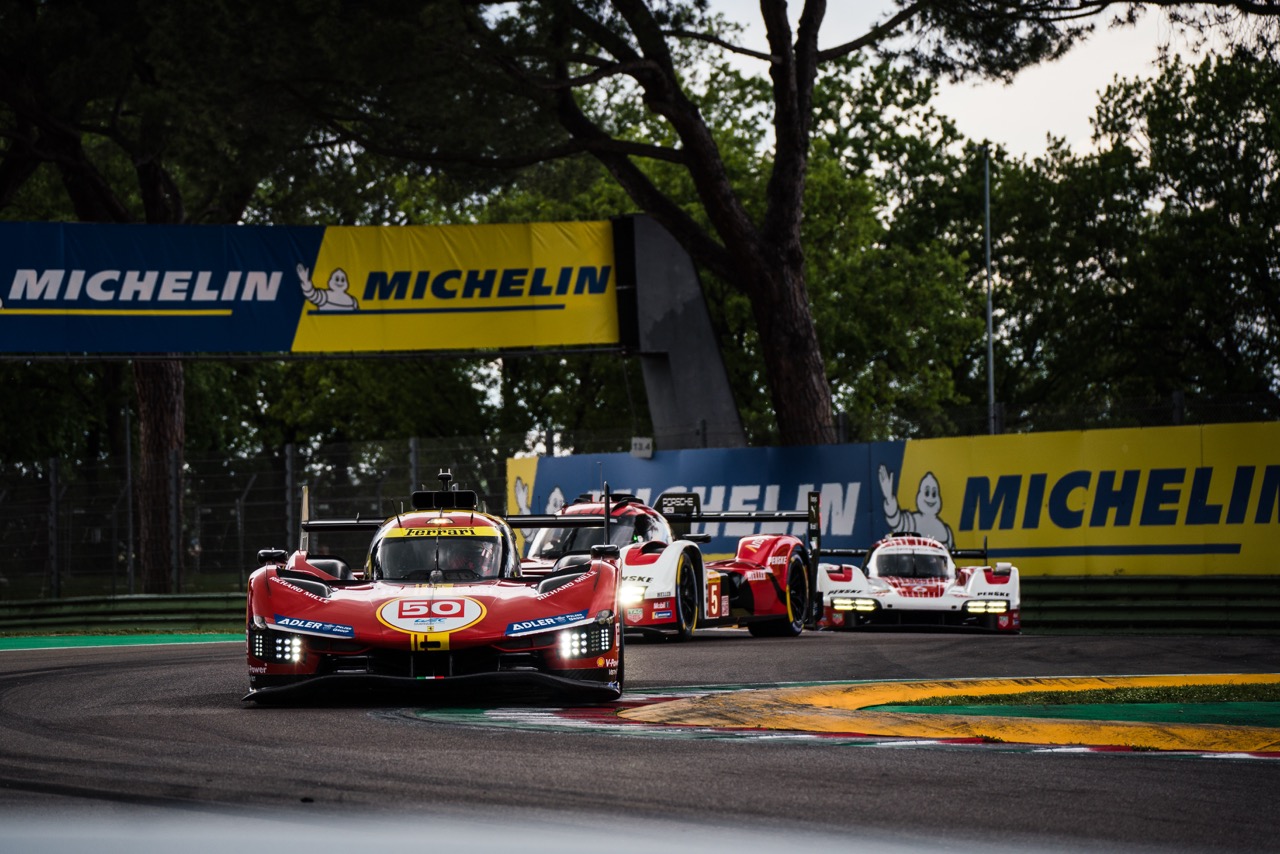 Race cars navigating a turn at the Imola Circuit, with a red car leading under Michelin banners