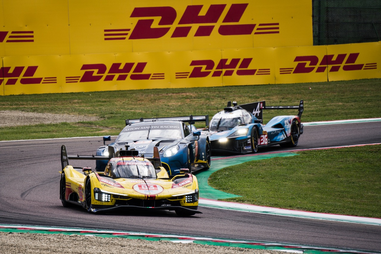 Three race cars navigate a corner at the Imola Circuit, passing DHL banners