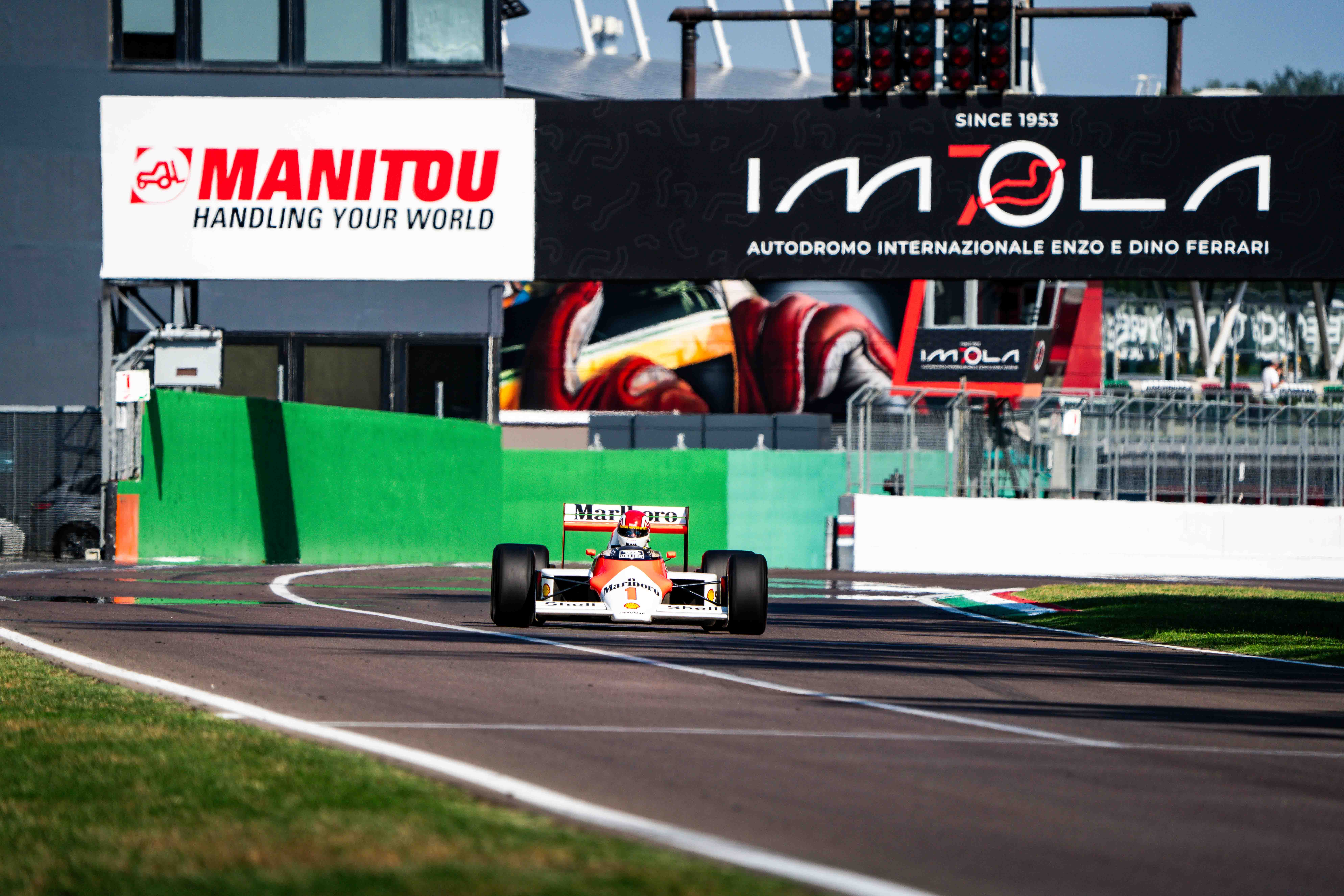 Front view of a vintage Formula 1 car racing at the Imola racetrack with trackside branding visible
