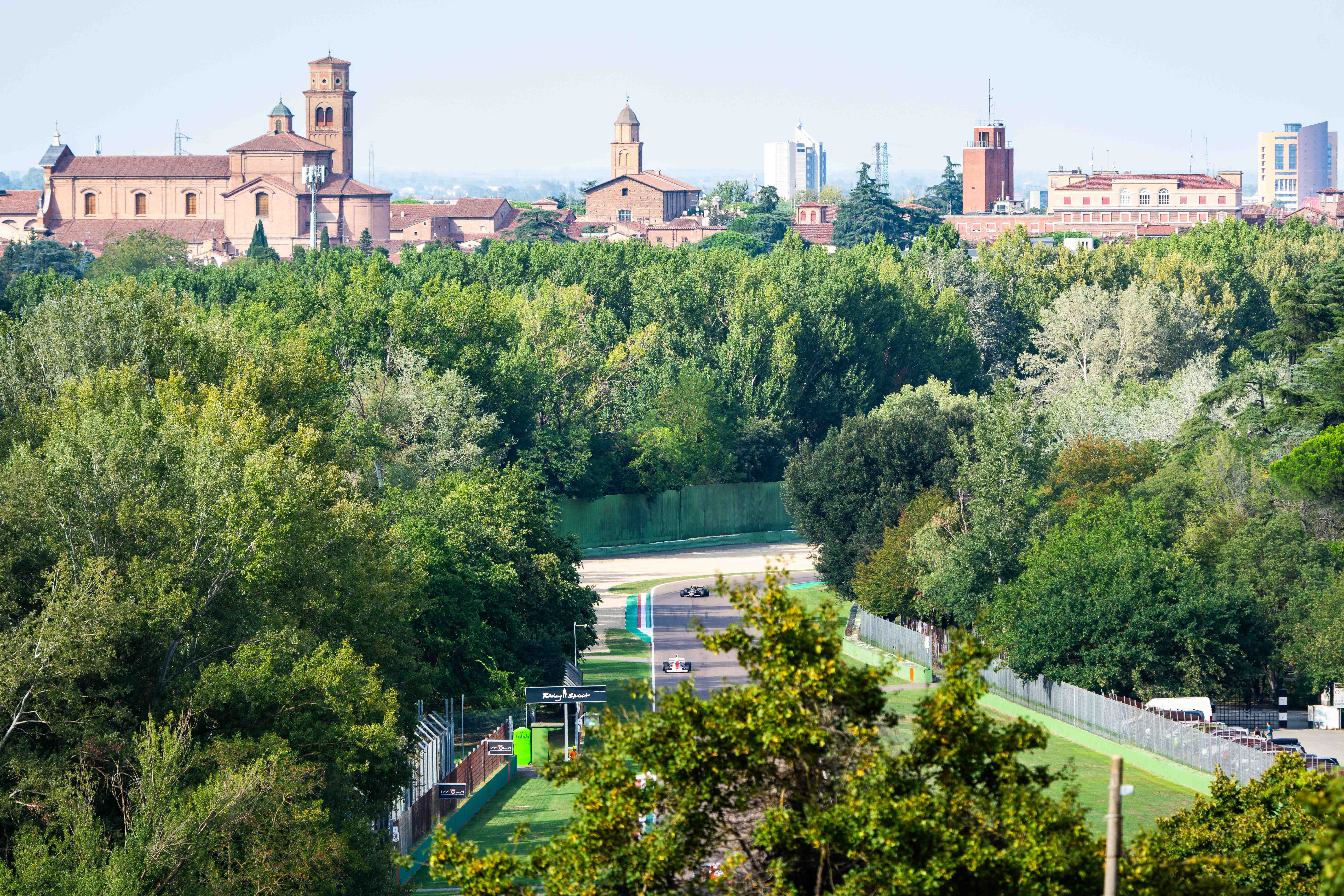 Scenic view of the Imola racetrack surrounded by lush greenery, with historic buildings in the background