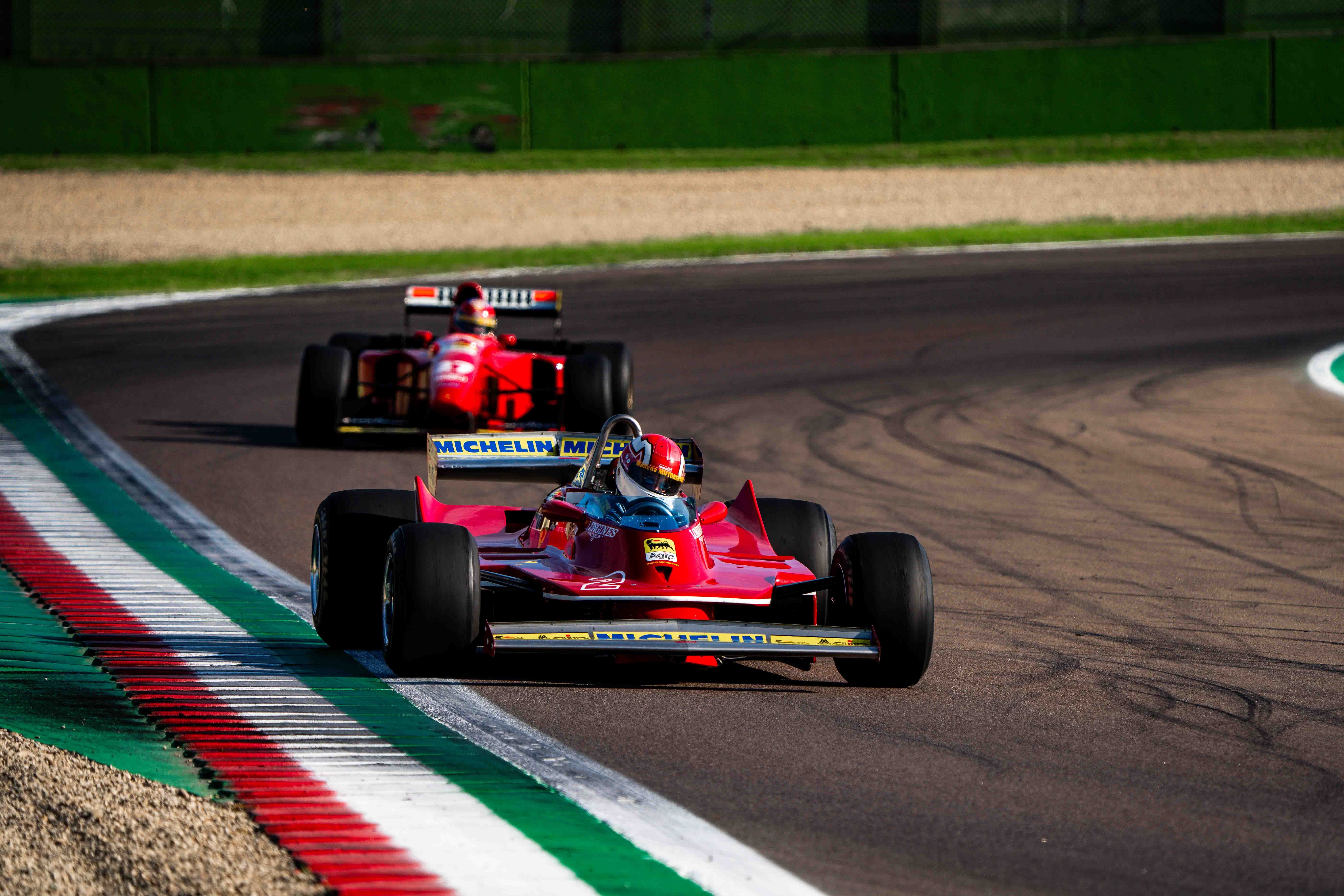 Two vintage Ferrari Formula 1 cars driving on a curve at the Imola racetrack under the afternoon sun