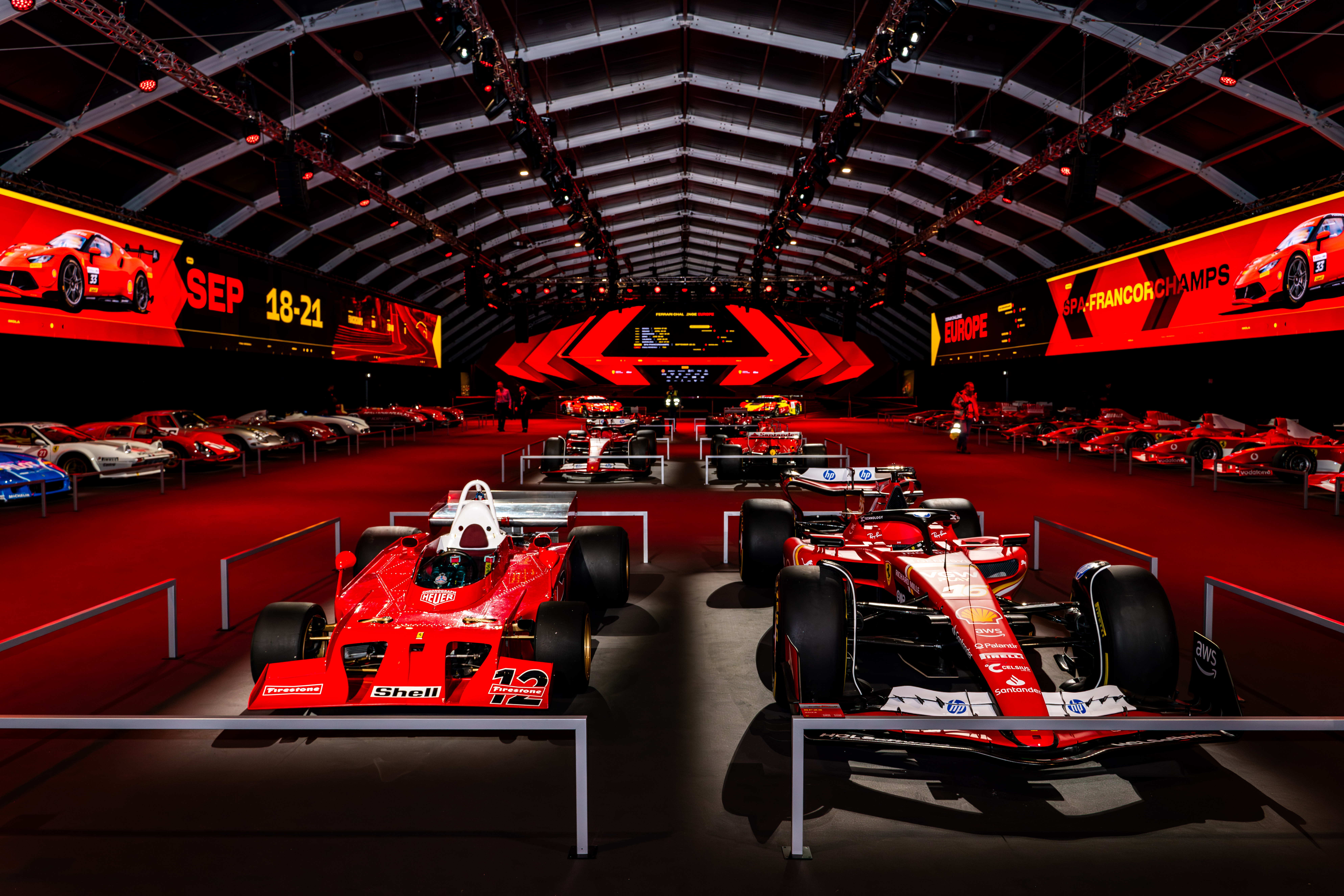 Exhibition hall showcasing iconic Ferrari Formula 1 cars with vibrant red lighting and digital displays