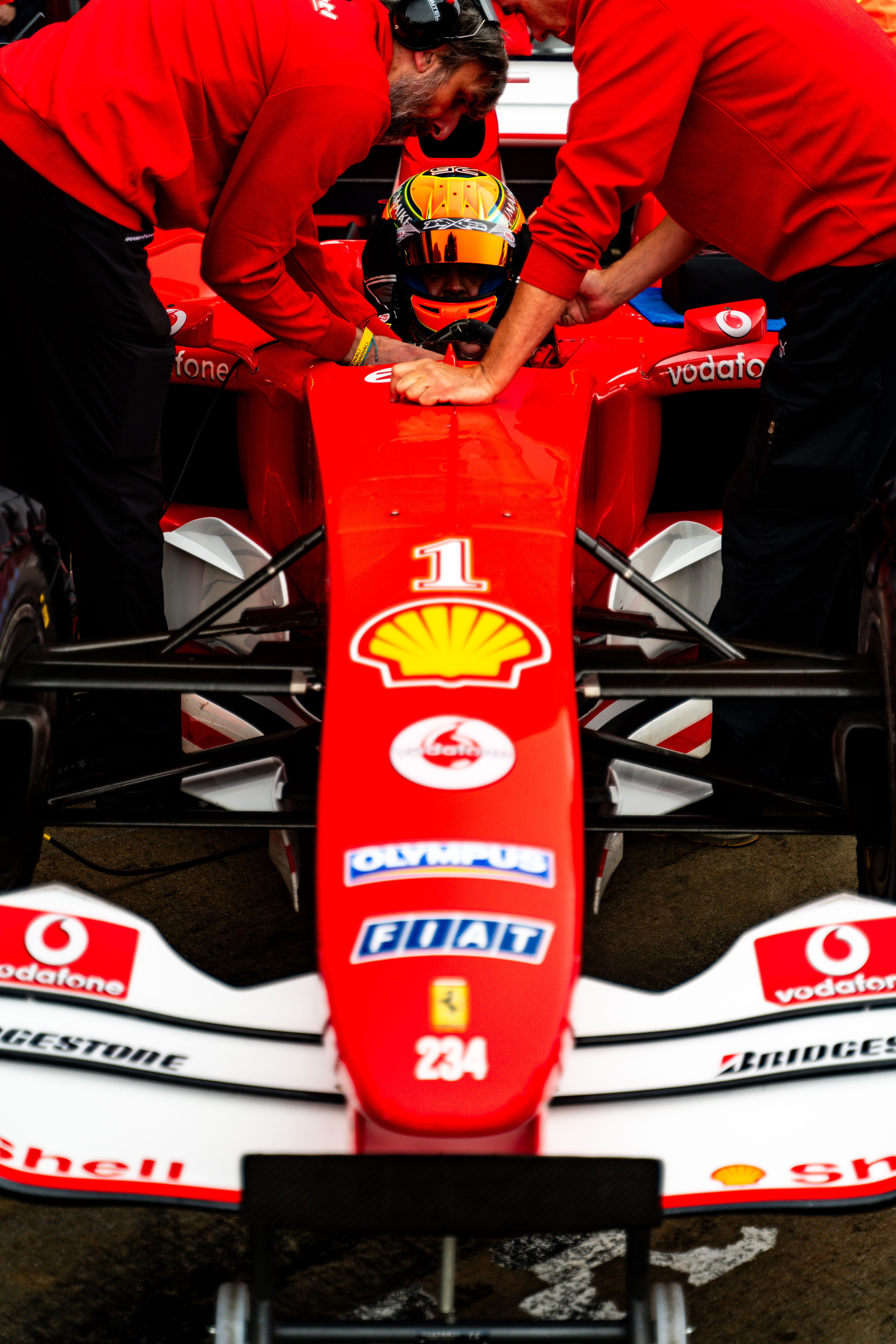 Ferrari Formula 1 driver being assisted into the car by two crew members during preparation