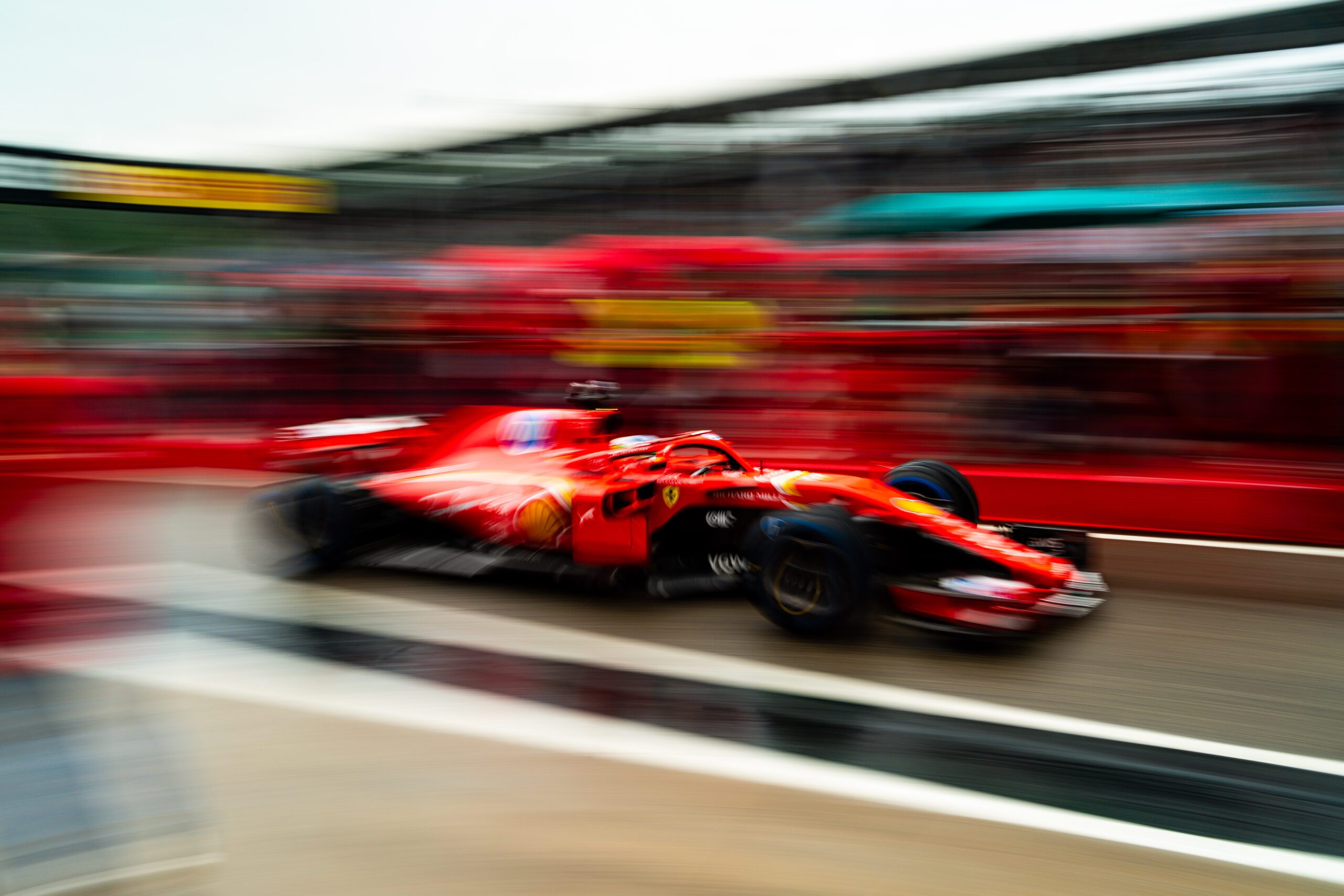 Side view of a Ferrari Formula 1 car racing out of the pit lane with motion blur against the background