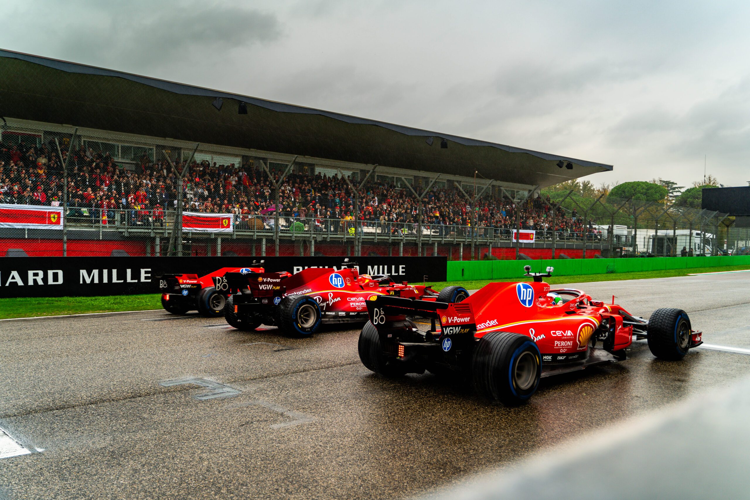 Three Ferrari Formula 1 cars lined up on a wet race track with spectators in the stands