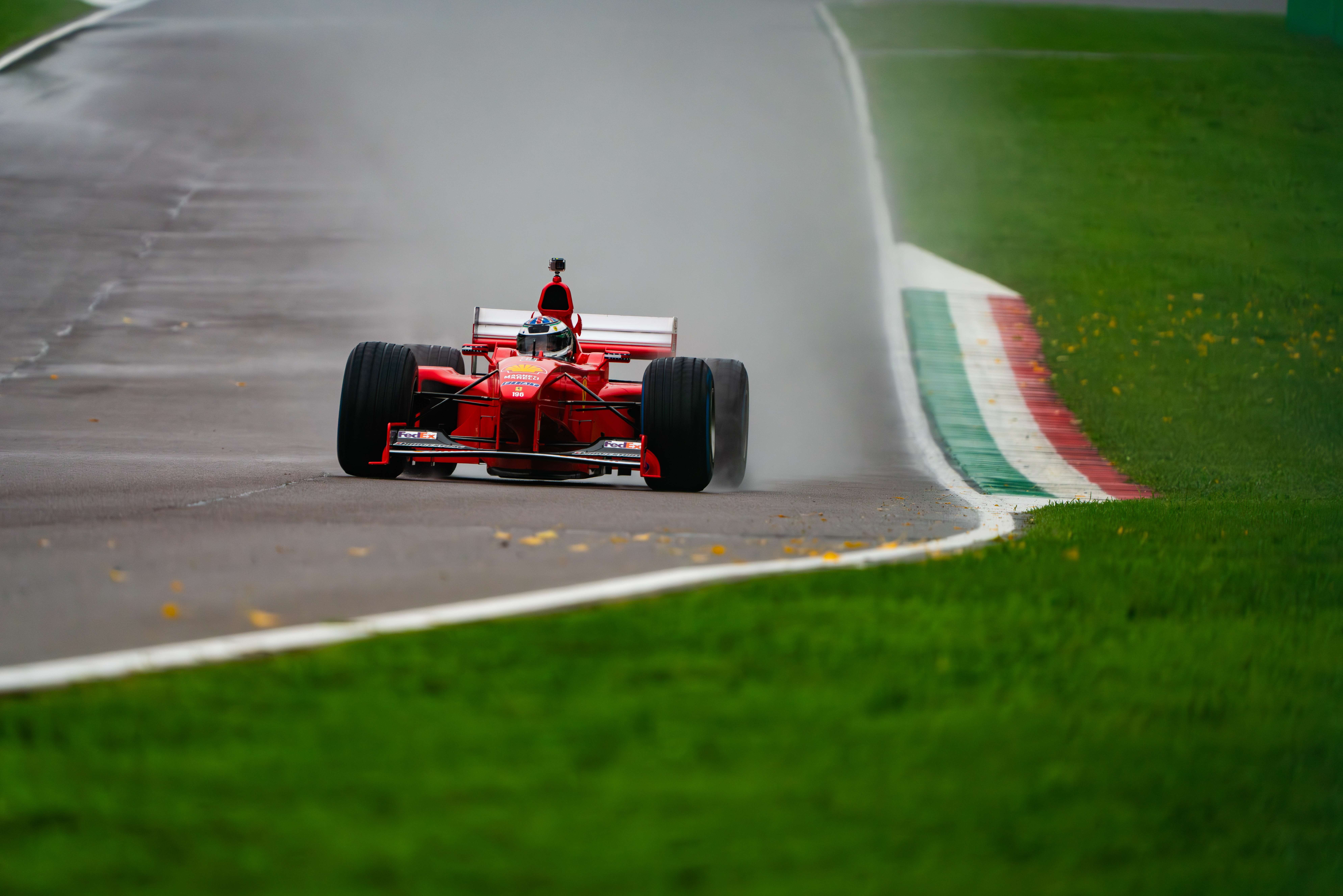 Ferrari Formula 1 car racing through a wet section of the Imola track, creating spray behind its wheels