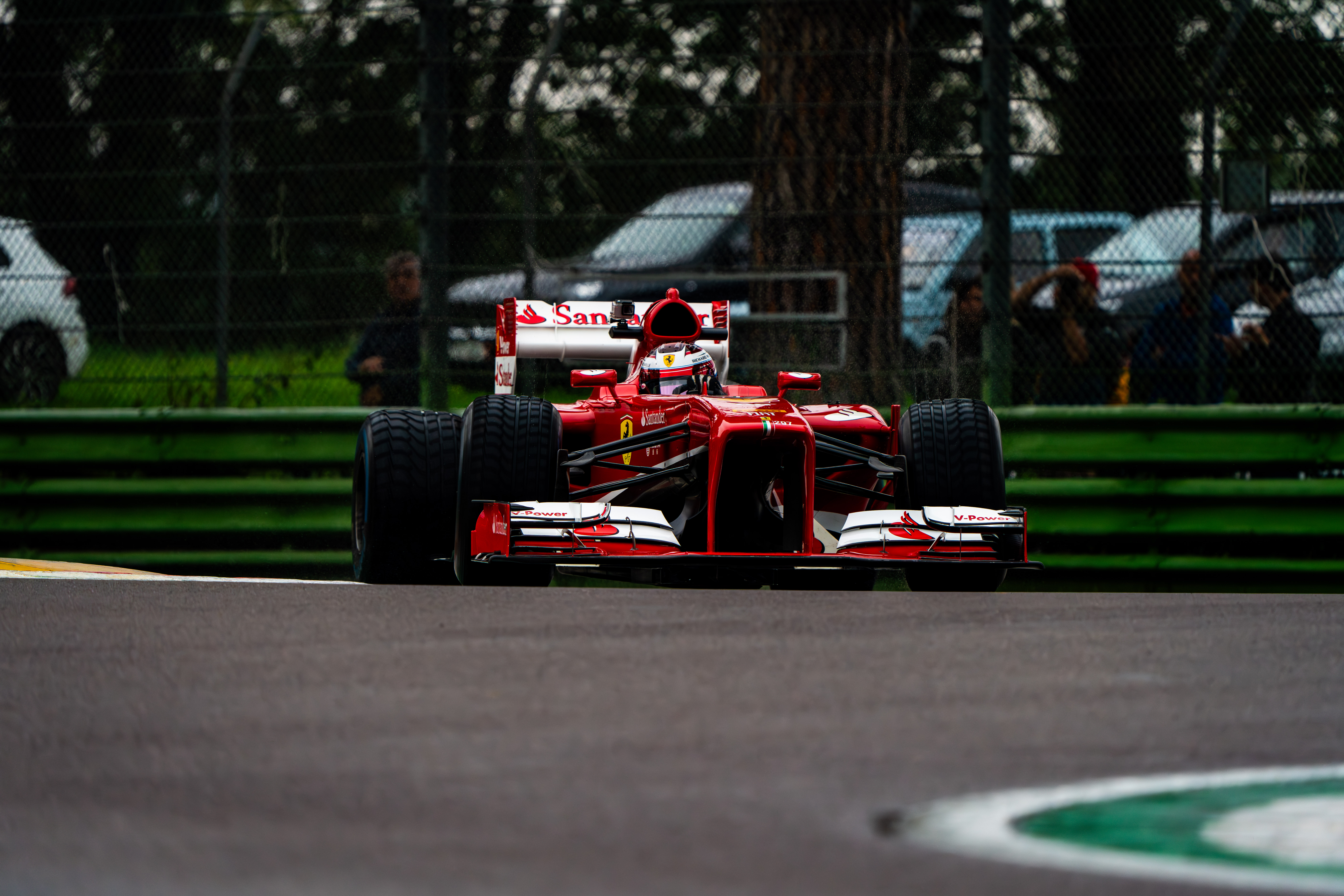 Front view of a Ferrari Formula 1 car on the track at Imola, with spectators and green fencing in the background